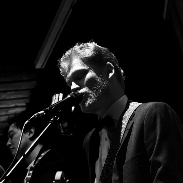 Der Gitarrist der Band Drahwurm singt ins Mikro und spielt auf seiner Gitarre in schwarz weiß