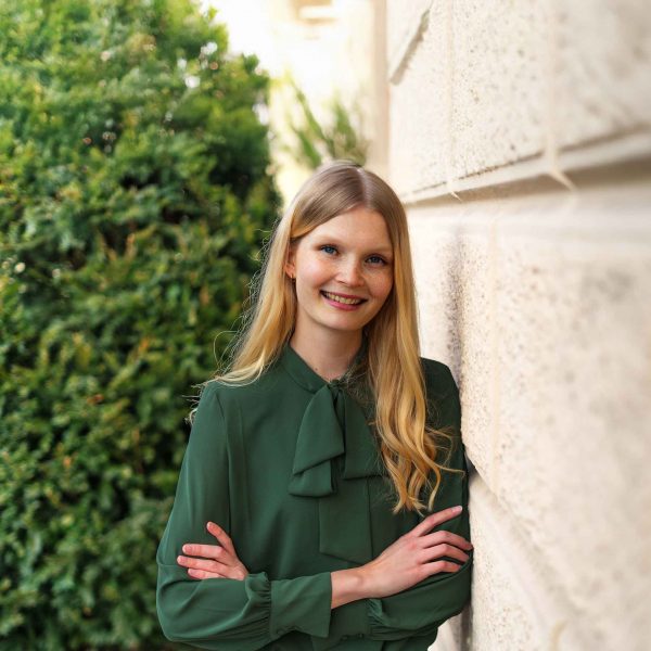 Frau mit Bluse lehnt an Mauer an und schaut in die Kamera