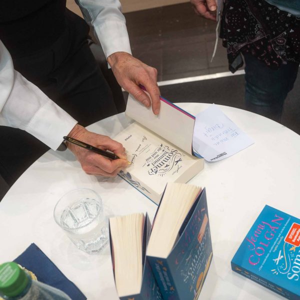 Ein Buch auf einem Tisch, da gerade signiert wird neben einem Glas Wasser und weiteren Büchern von Jenny Colgan