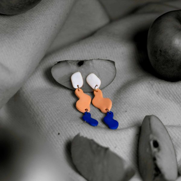 Ein Foto in Schwarz Weiß bis auf ein farbiges Paar Ohrringe das iin der Mitte in einem Stueck Apfel steckt