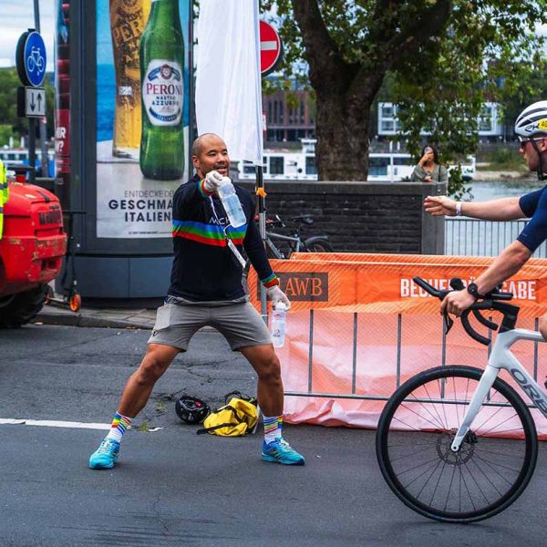 Ein Man übergibt einem Rennradfahrer eine Wasserflasche auf der Rennstrecke